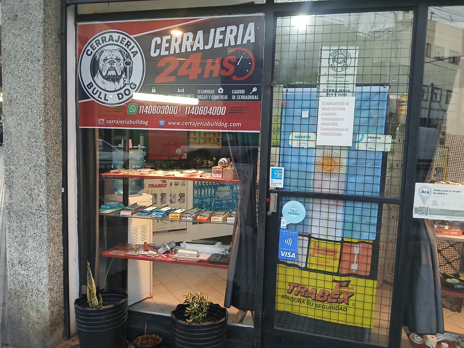 Fachada de Cerrajería Bulldog de día — cartel 24HS, logo Bulldog, TRABEX y medios de pago